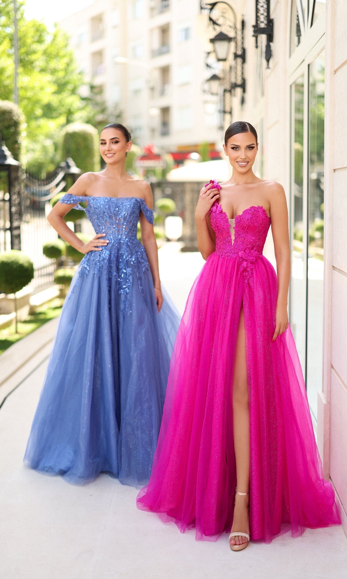 Two women stand outdoors in formal gowns; one smiles in the Long Glitter Blue Prom Dress: Tina Holly TE232, an off-the-shoulder style, while the other wears a strapless pink high-slit dress. Both look at the camera.